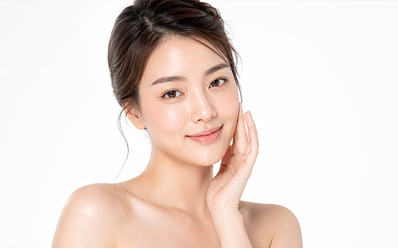 Asian woman touching her clear glowing cheek with a radiant smile.