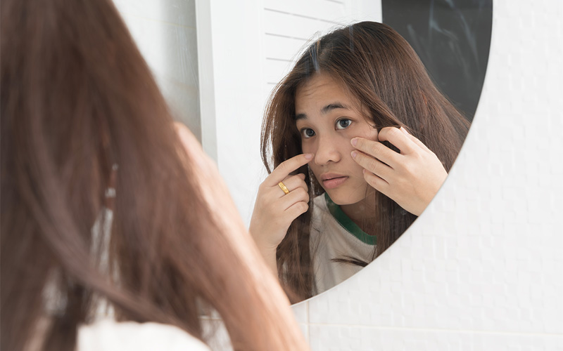 Woman looking in mirror examining dull and uneven skin texture